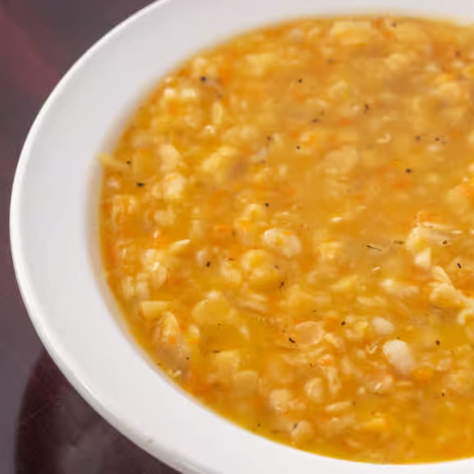 Close-up of a white bowl filled with a hearty, golden-orange Lebanese lentil soup.