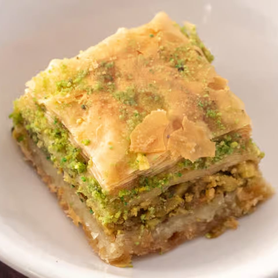 Close-up of a square piece of baklava, layered with golden pastry and green pistachio filling.