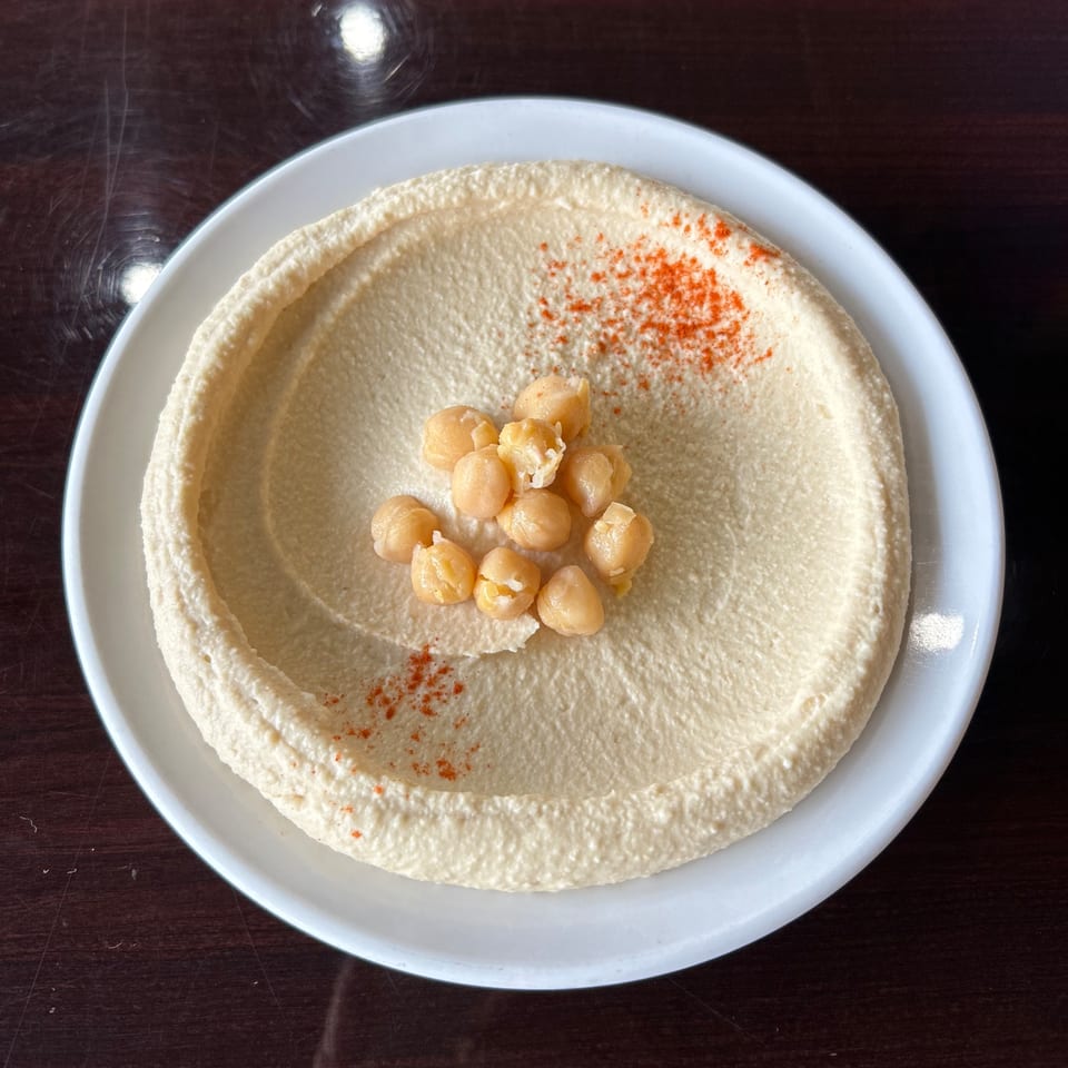 Creamy Lebanese hummus in a white bowl, garnished with whole chickpeas and paprika.
