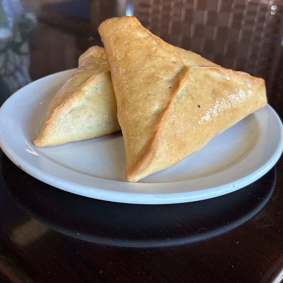 Two golden-brown, triangular Lebanese fatayer pastries on a white plate at La Mia Restaurant.