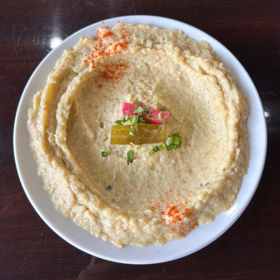 Creamy Lebanese baba ghanoush topped with paprika, pickled vegetables, and fresh parsley on a white plate.