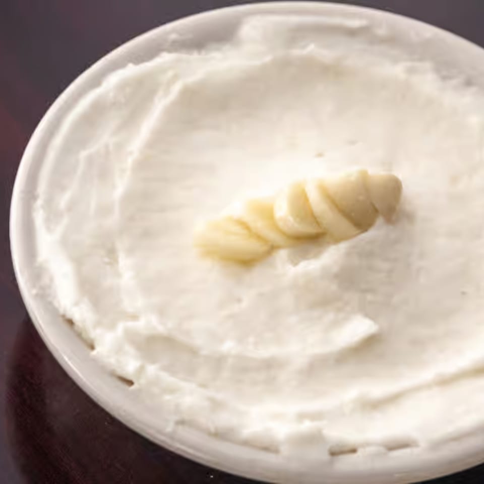 A white bowl of creamy Lebanese garlic dip, toum, garnished with garlic cloves.