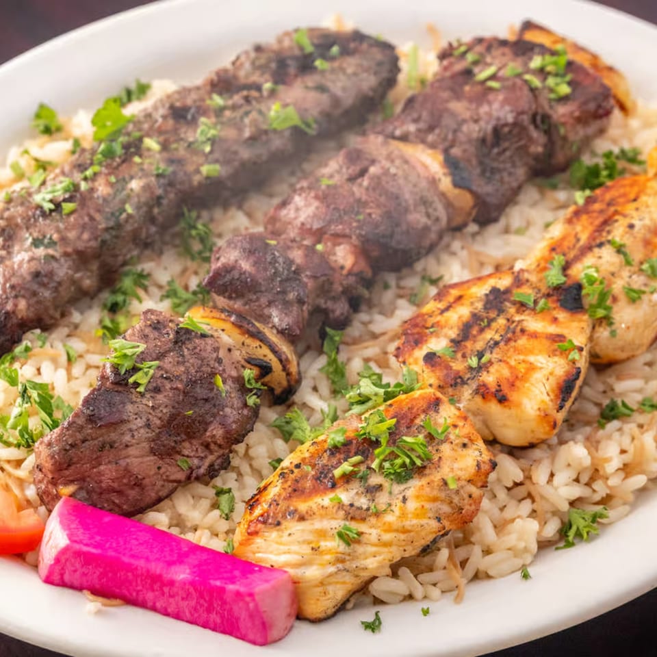 Lebanese mixed grill plate with beef and chicken skewers, rice, and pink pickled turnips.