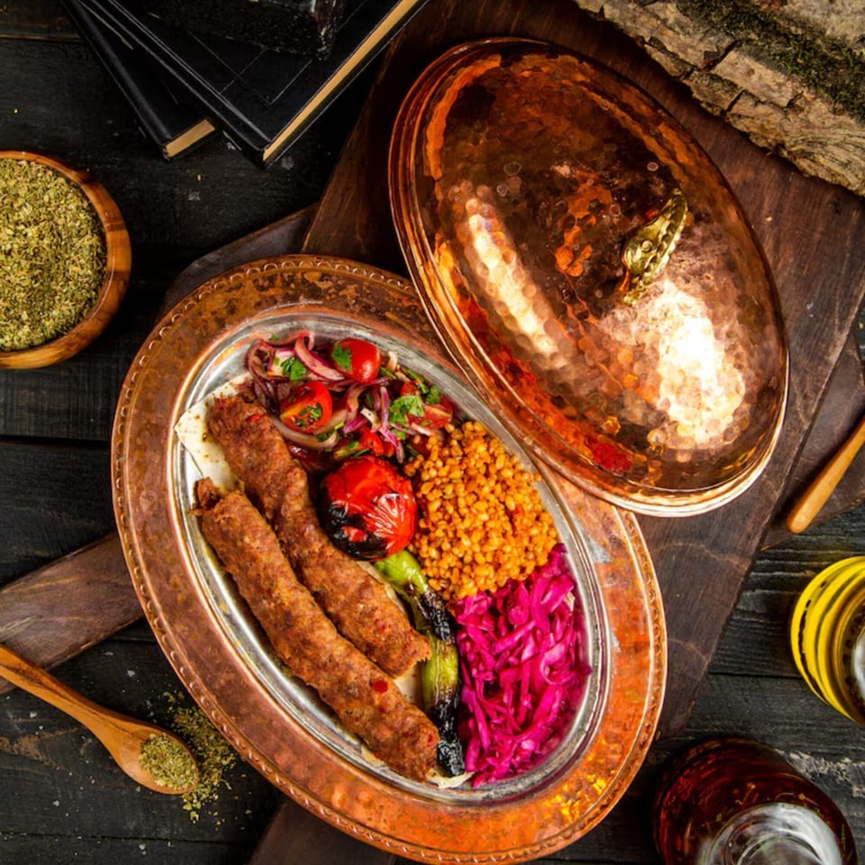 Lebanese kofta kebabs with bulgur, grilled vegetables, and pickled cabbage on a copper platter.